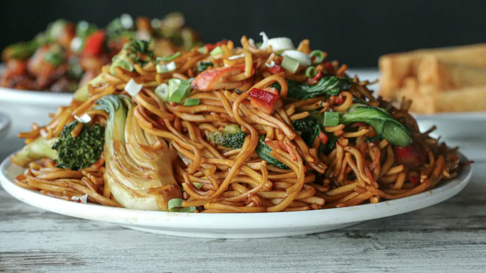A plate of stir-fried noodles with broccoli, bok choy and green onions