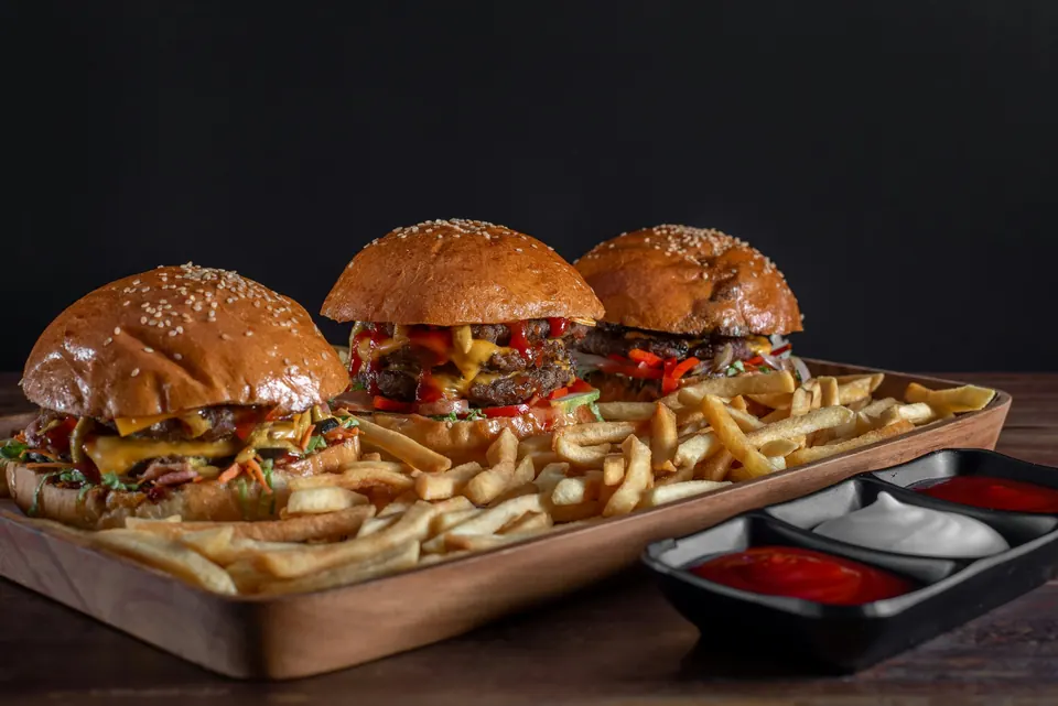 Three burgers on a board with fries and small dishes of dipping sauce