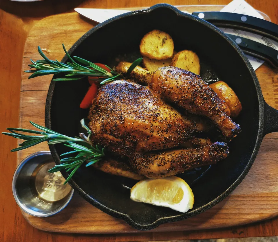 A whole roast chicken with rosemary, potatoes and lemon in a cast-iron skillet