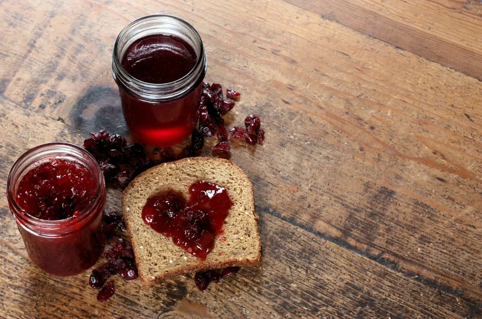 Jars of homemade berry jam beside a slice of toast spread with jam in a heart shape