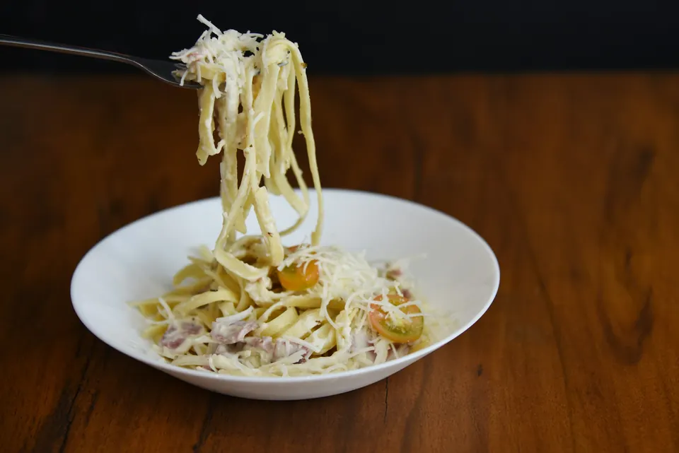 Fettuccine being lifted from a white bowl with a fork