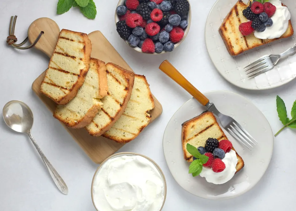 Slices of pound cake on a board with berries, whipped cream and plated servings