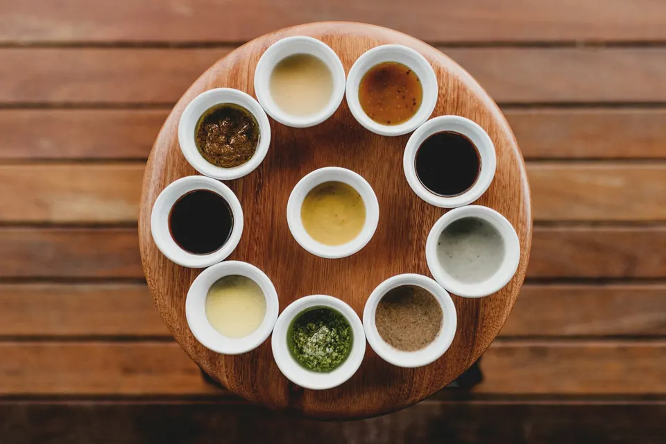 A round wooden board holding small white bowls of different sauces and dips