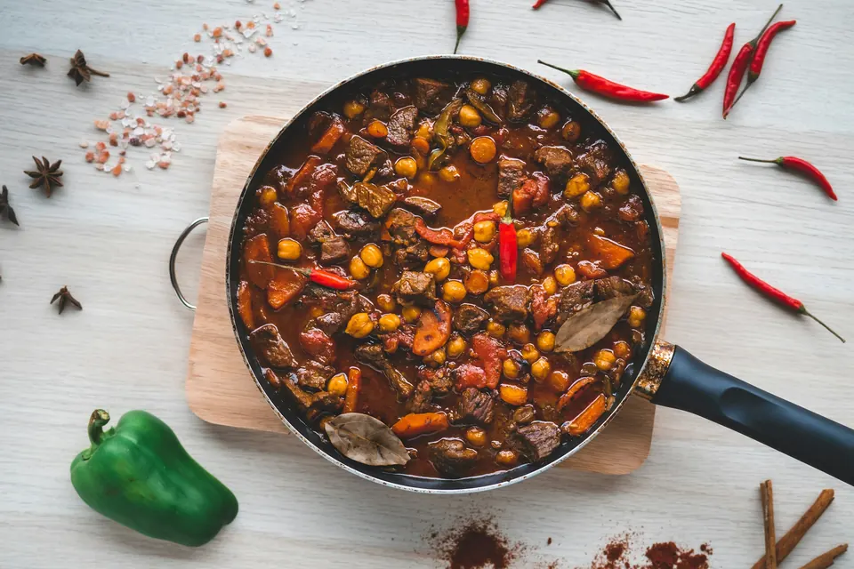 A pan of chili with beans and peppers beside fresh red chilies and a green pepper