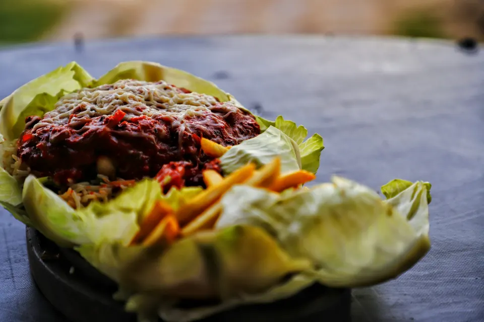 A lettuce cup filled with saucy ground meat, cheese and shredded carrots