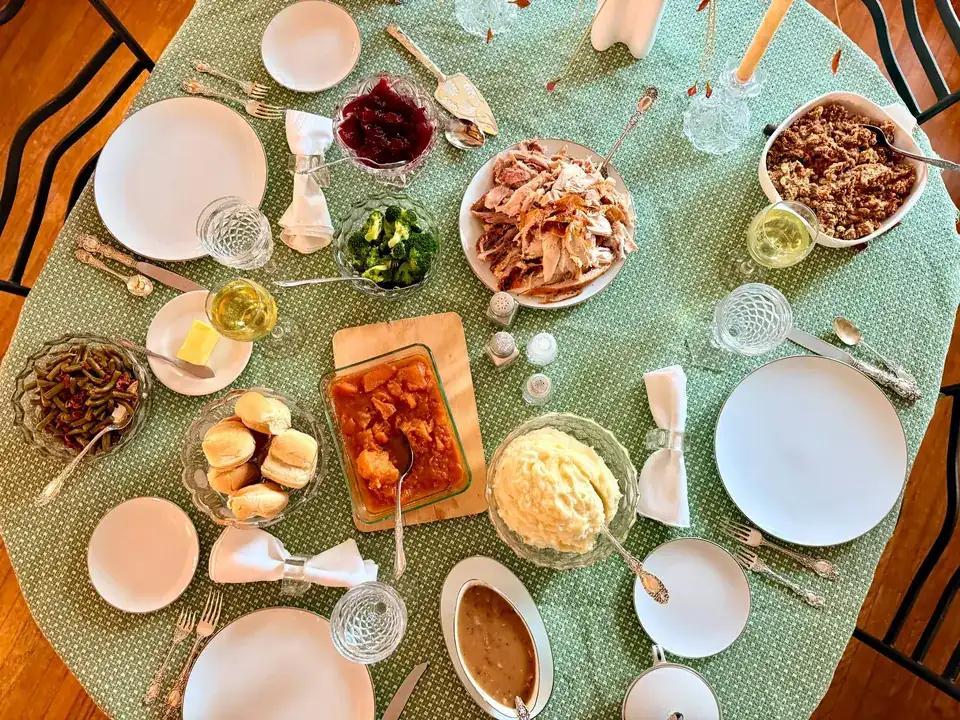 An overhead view of a family dinner table laid with roast turkey, sides, sauces and bread rolls on a green tablecloth