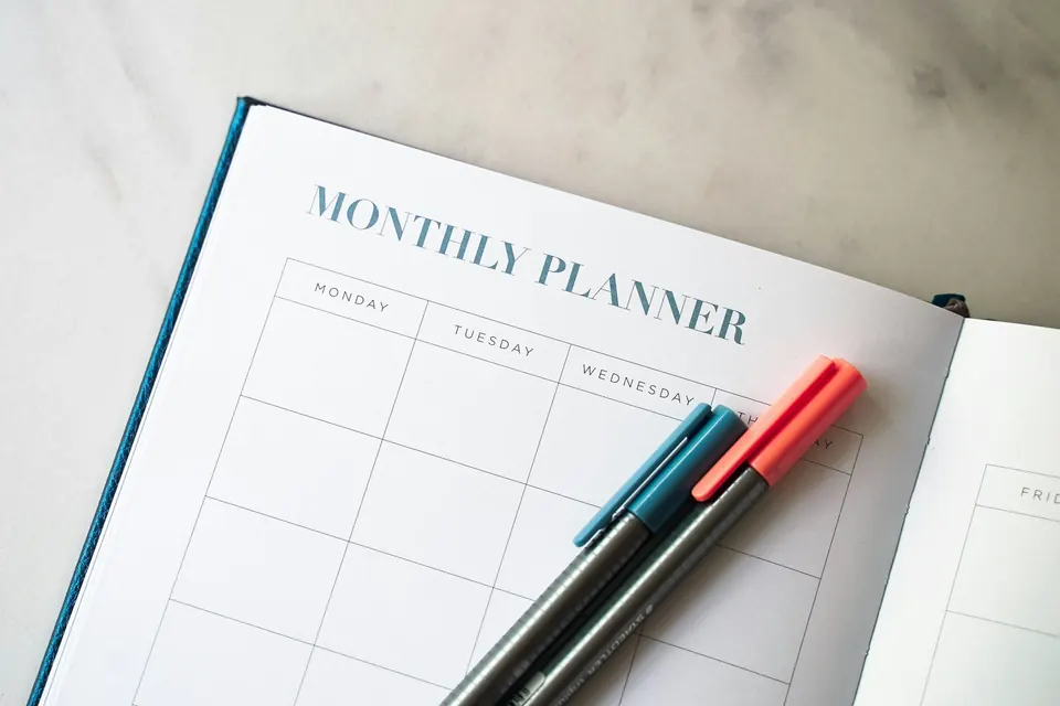 An open monthly planner with two pens on a marble table