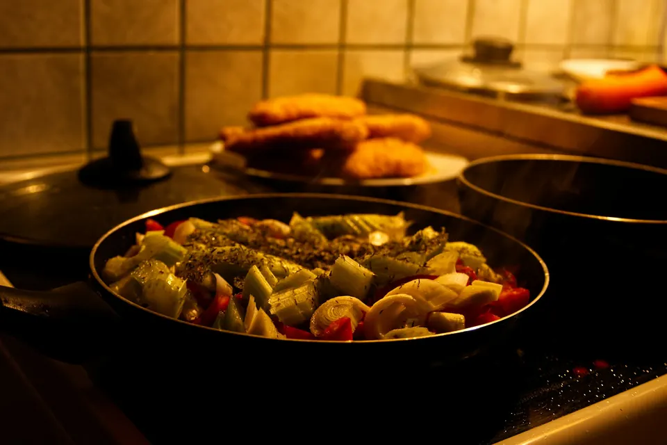 A pan of vegetables cooking on a stovetop in a warmly lit home kitchen