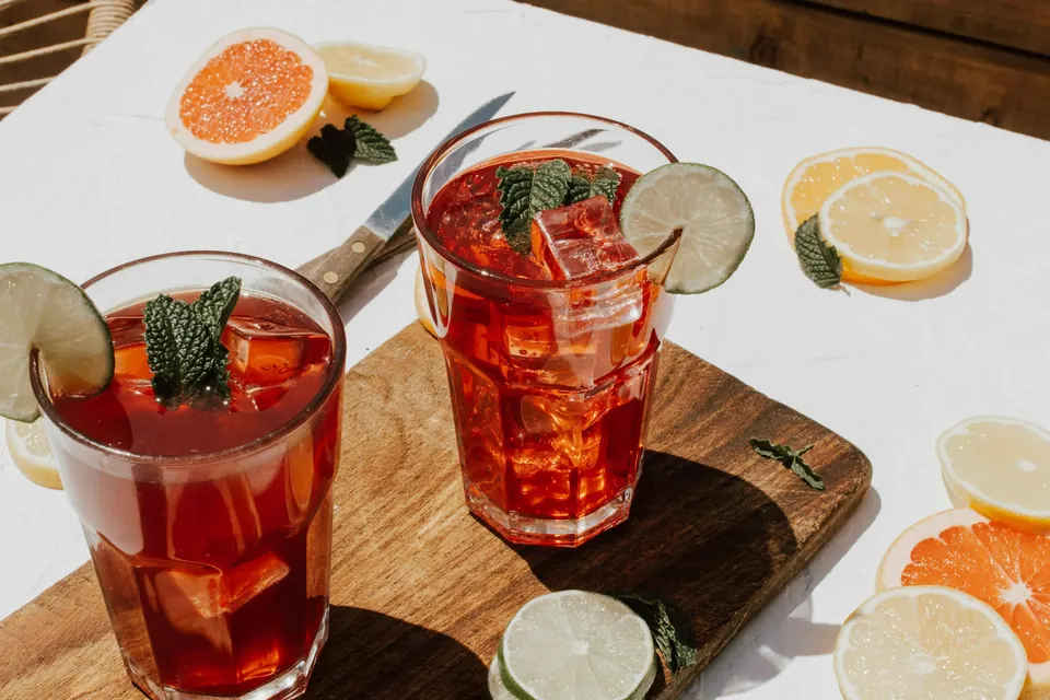 Two iced drinks with mint and citrus slices on a wooden board