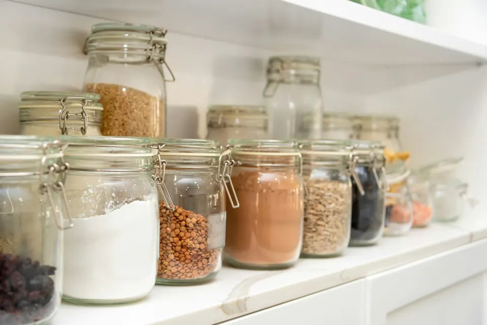Glass storage jars of flour, grains, lentils and spices on a pantry shelf