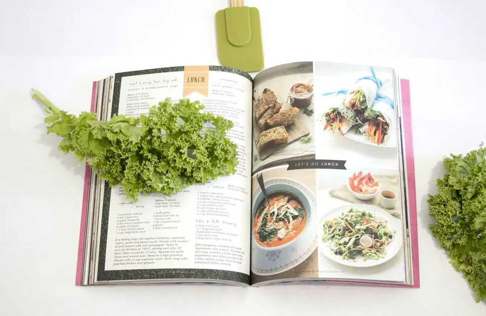 An open cookbook with recipe photos beside fresh kale