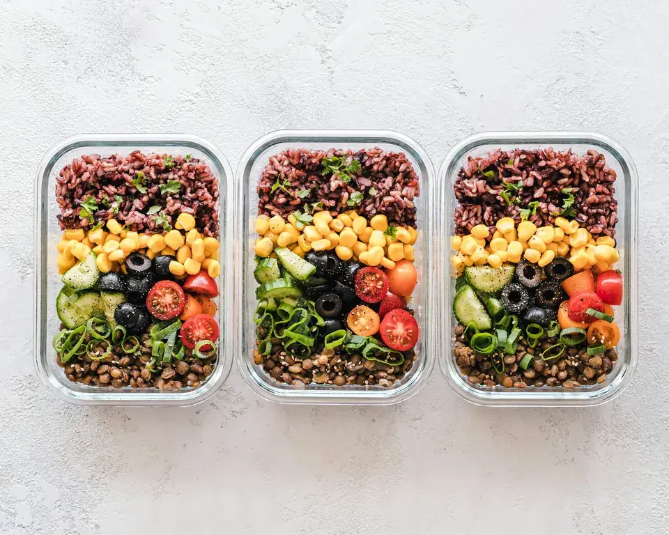 Three glass meal-prep containers filled with grains, chickpeas, tomatoes and olives