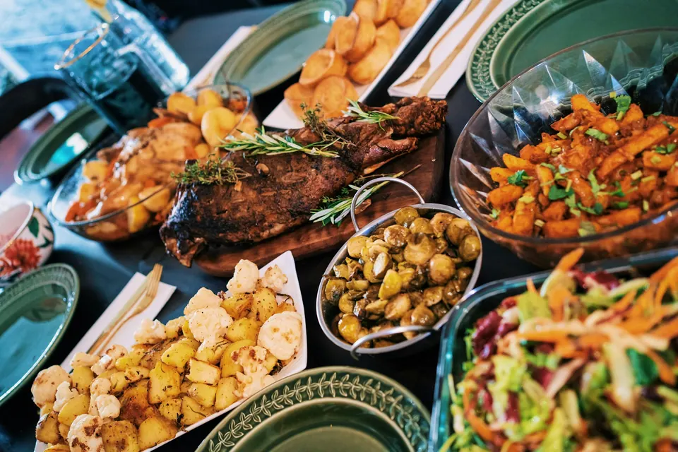 A table spread with a roast, roasted potatoes, glazed carrots, salads and sides in green dishes