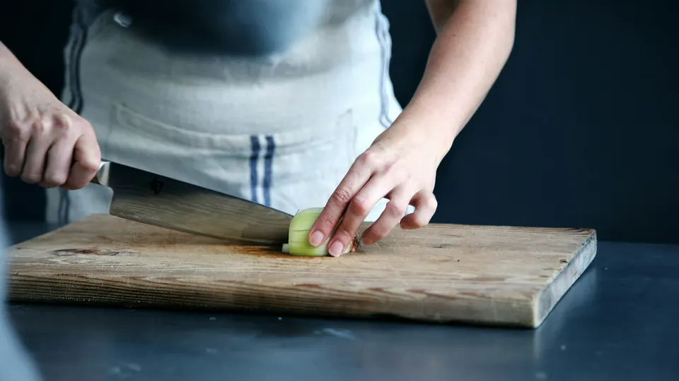 A cook slicing a vegetable on a wooden chopping board