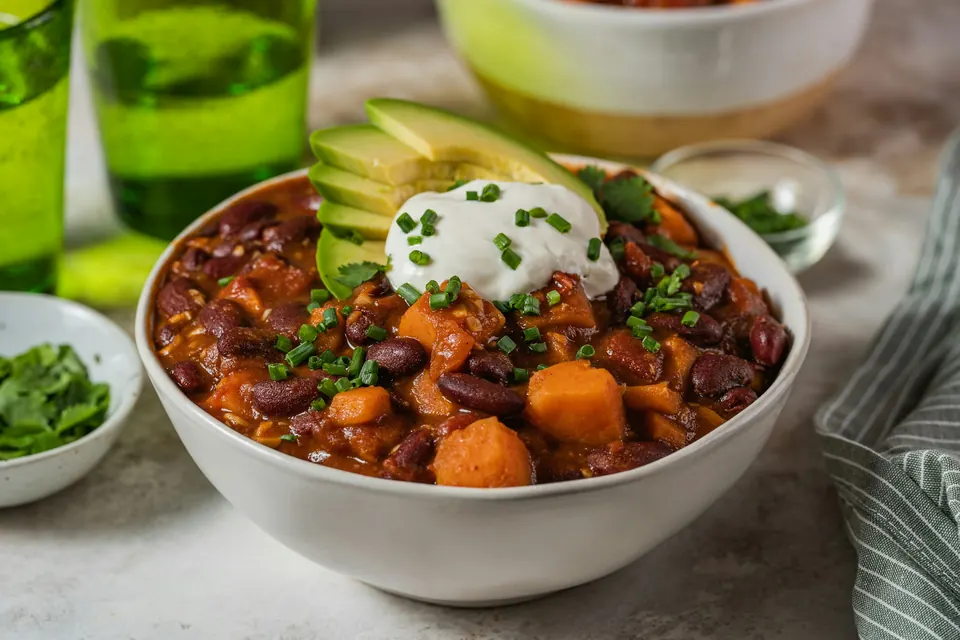A bowl of bean and sweet potato chili topped with sour cream, avocado and chives