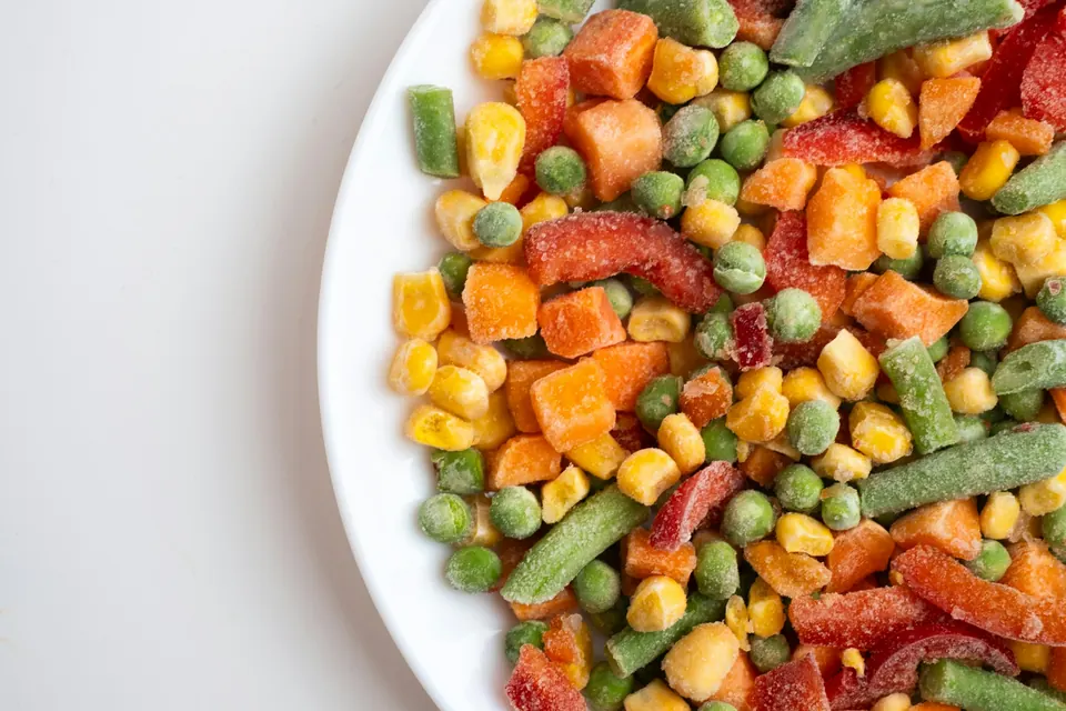 Frozen mixed vegetables with peas, corn, carrots and green beans on a white plate