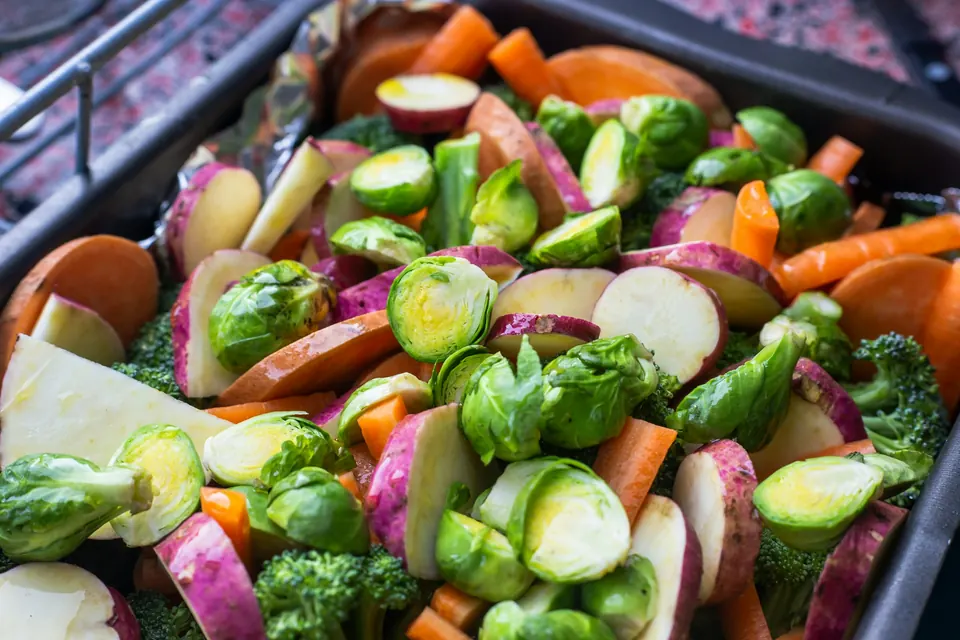 Brussels sprouts, carrots, radishes and broccoli ready to roast on a dark tray