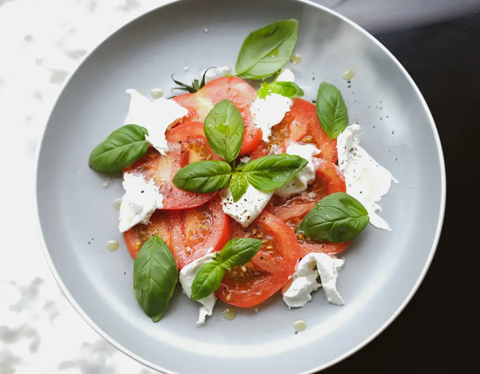 A caprese salad of sliced tomatoes, torn mozzarella and basil on a grey plate